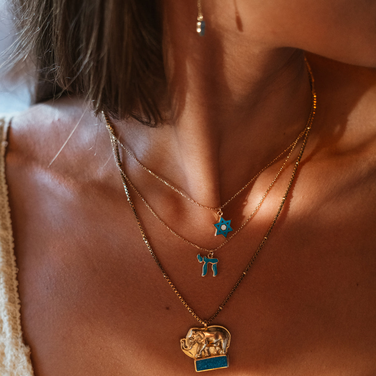 Lucky Elephant Turquoise Mosaic Gold Pendant Necklace layered with two fine turquoise pendant necklaces in warm light