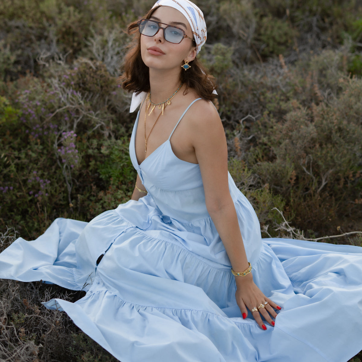 Woman seated outdoors in a pale blue dress and headscarf wearing the Lucky Fish turquoise beaded necklace