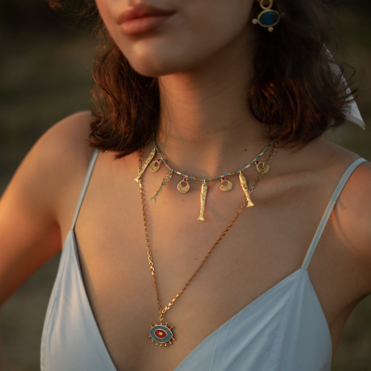 Model in sunglasses and a headscarf at sunset wearing the Lucky Fish beaded necklace with a gold evil eye pendant