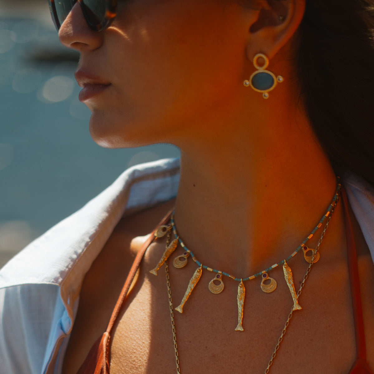 Close up of the Lucky Fish turquoise beaded necklace worn at the base of the throat with the Cleopatra Blue Cat's Eye gold stud earrings