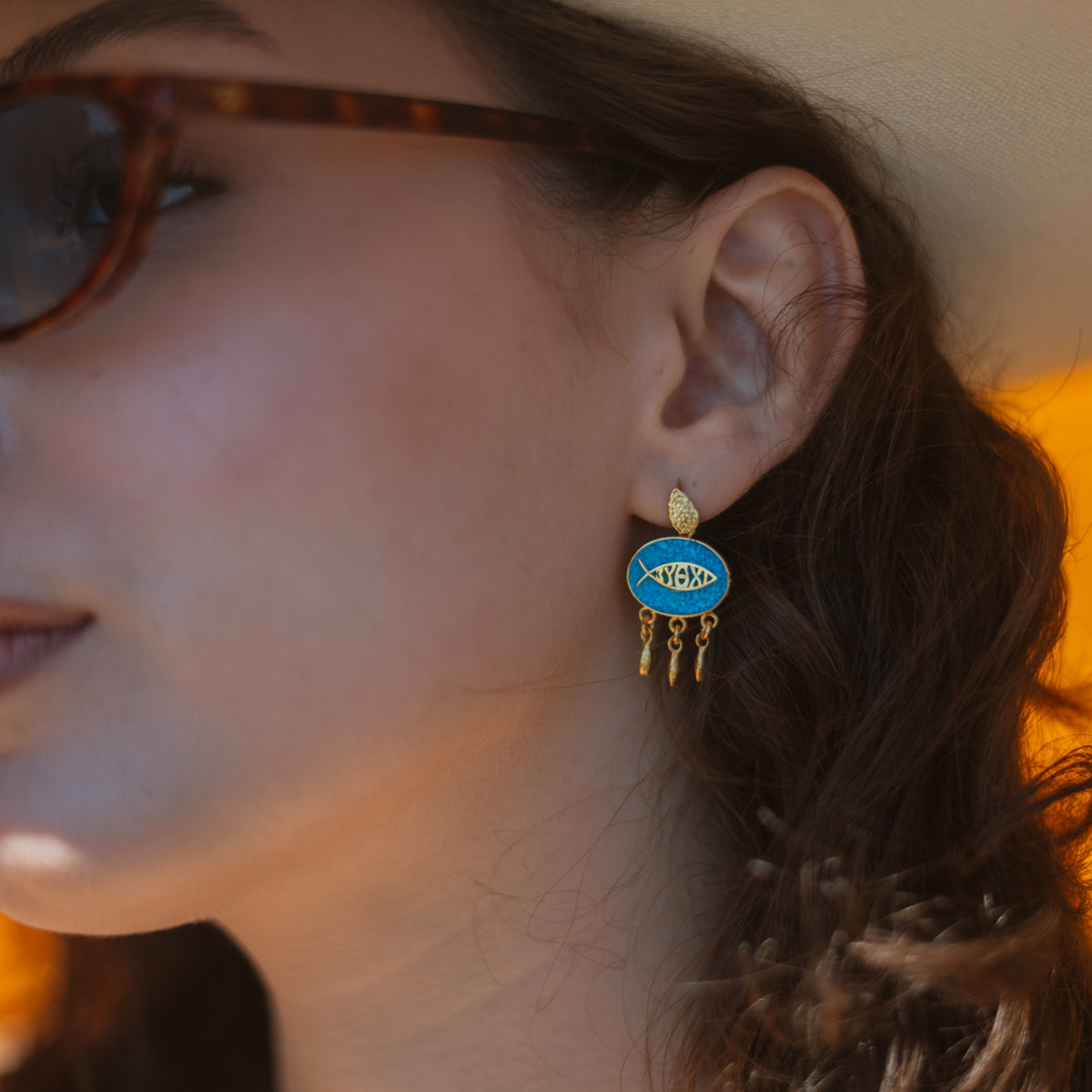 Close up of a turquoise mosaic lucky fish gold drop earring worn on the ear