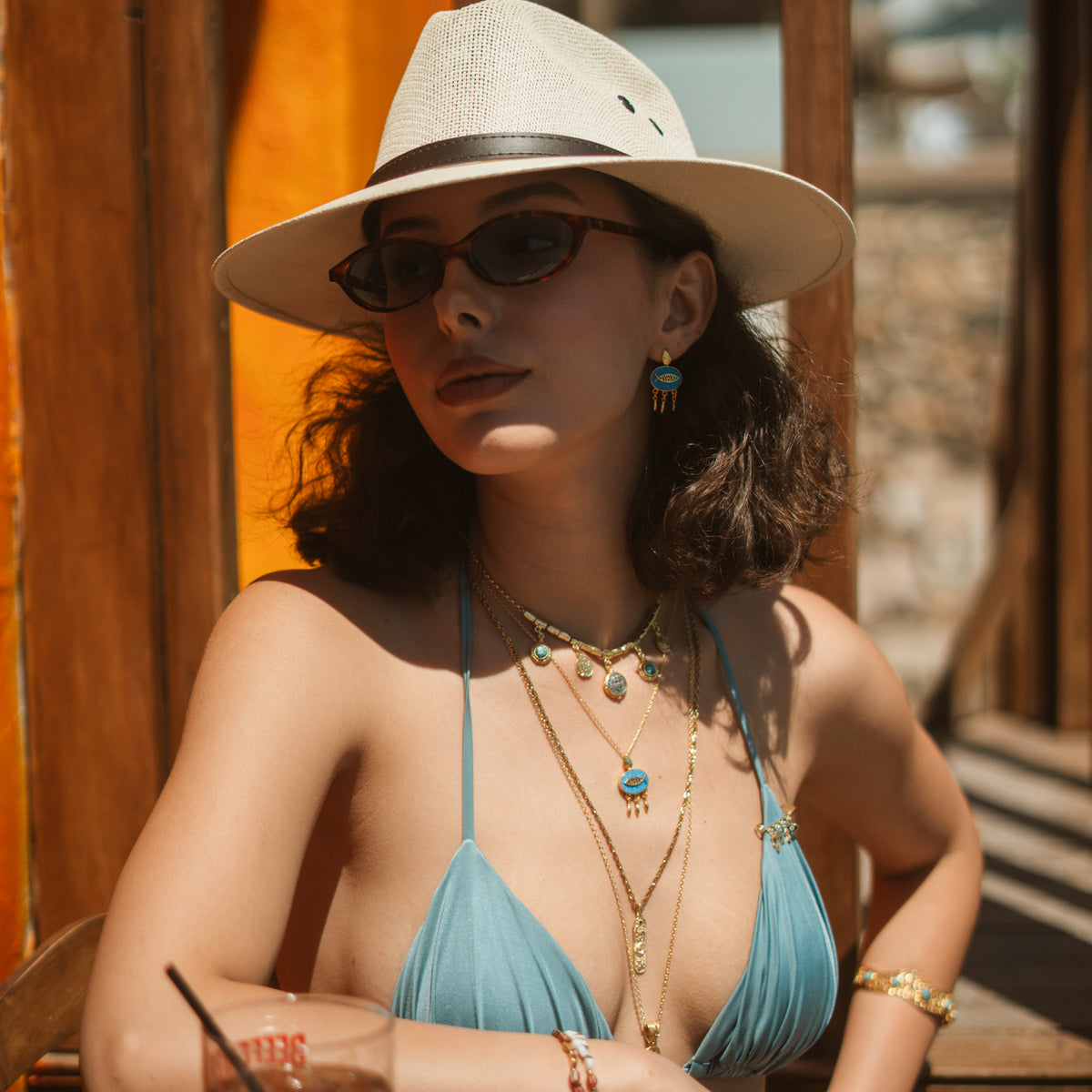Woman on a sunny terrace wearing turquoise mosaic lucky fish gold drop earrings