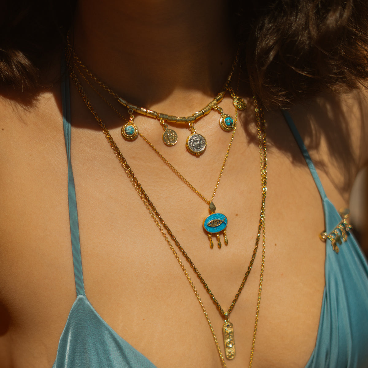 Close view of the lucky fish turquoise mosaic pendant layered under a coin charm choker in warm sunlight