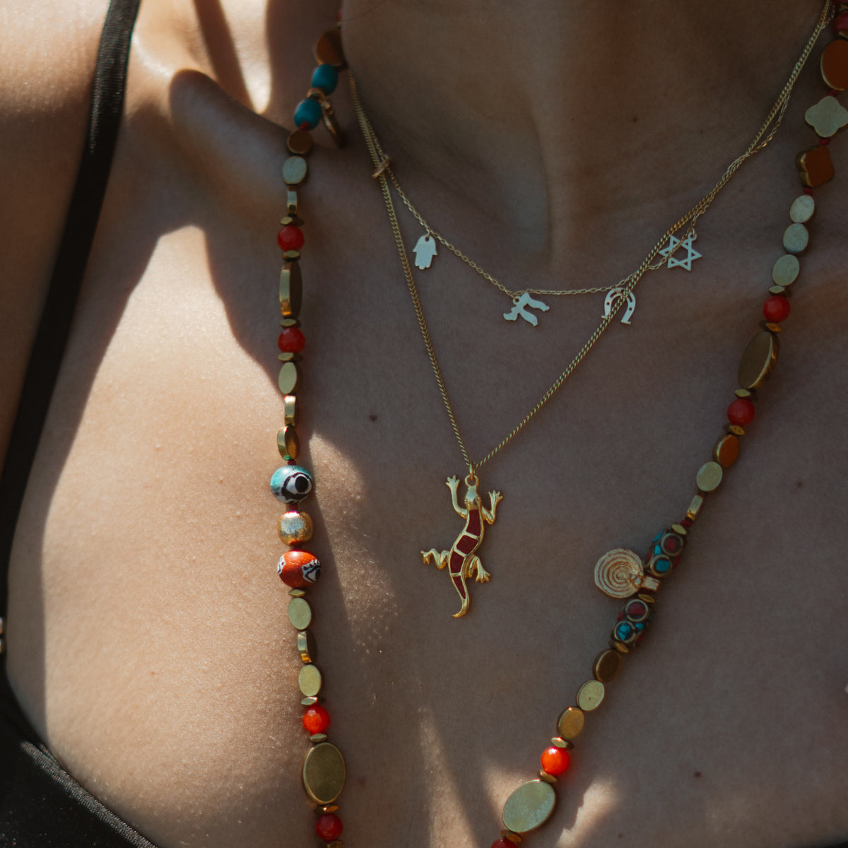 Lucky Gecko Red Enamel Gold Pendant Necklace on the collarbone, layered with a gold charm necklace and a long beaded necklace