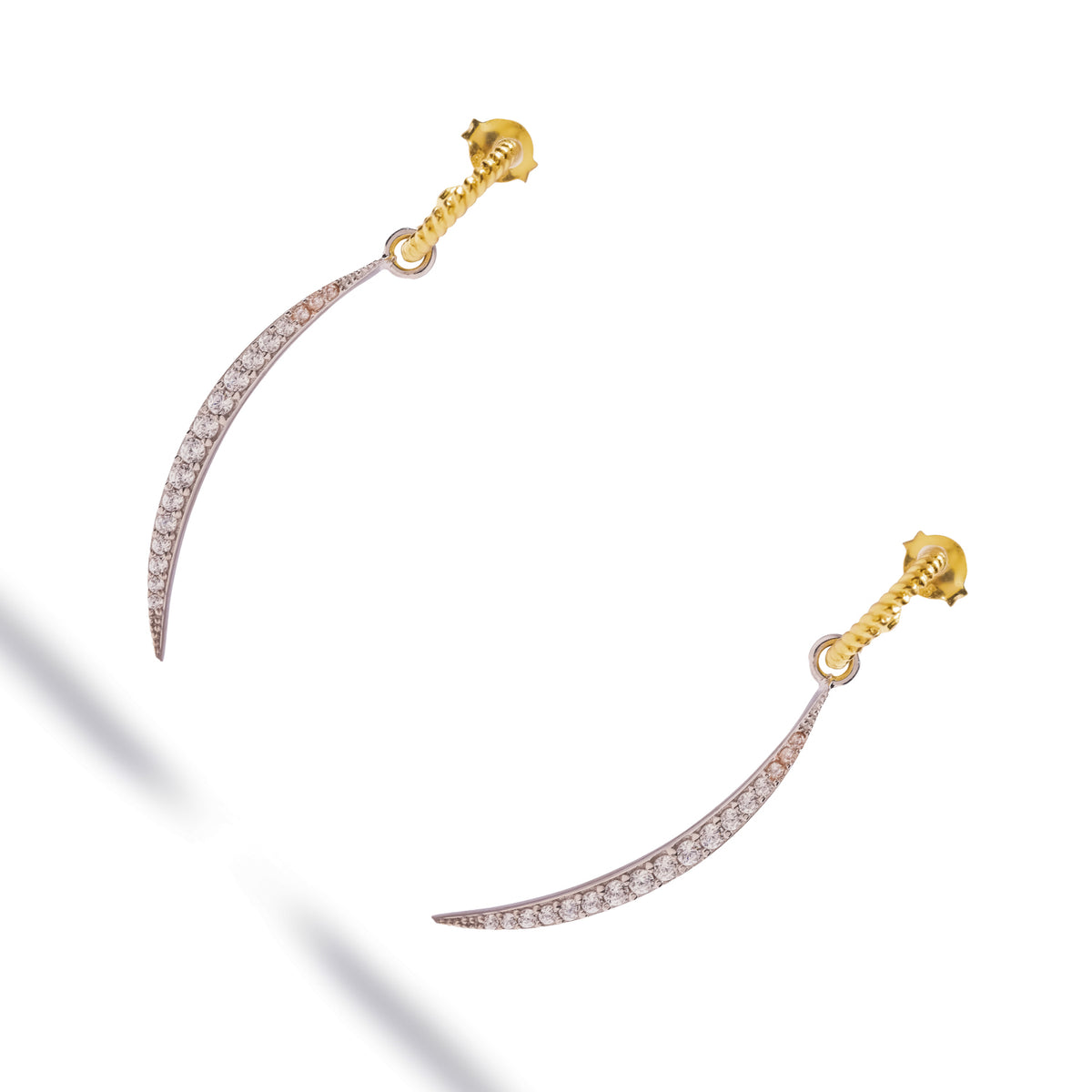 Pair of mixed metal pave zircon arc drop earrings laid at an angle on white