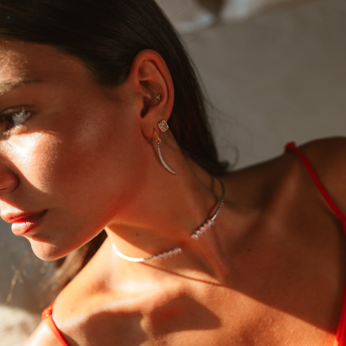Close view of the Luminous Arc earring on the ear in warm light, worn with a silver marquise choker
