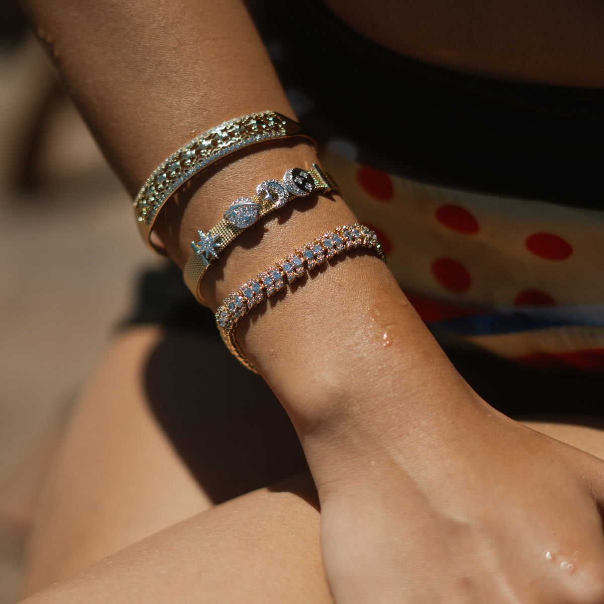 Luminous Halo zircon tennis bracelet stacked with a gold cuff and a charm bracelet in sunlight