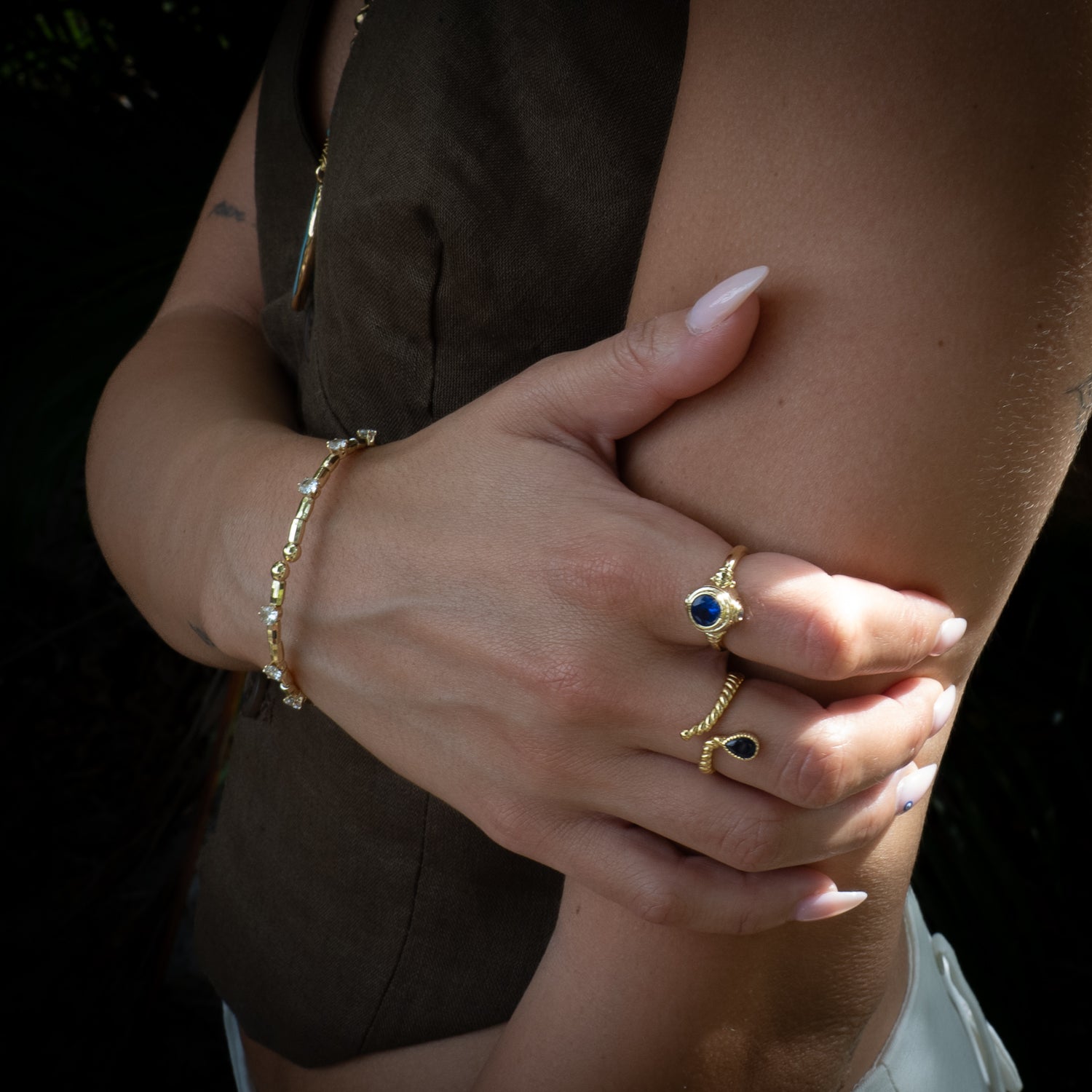 Close-up of a person's arm with gold jewelry including a bracelet, ring.