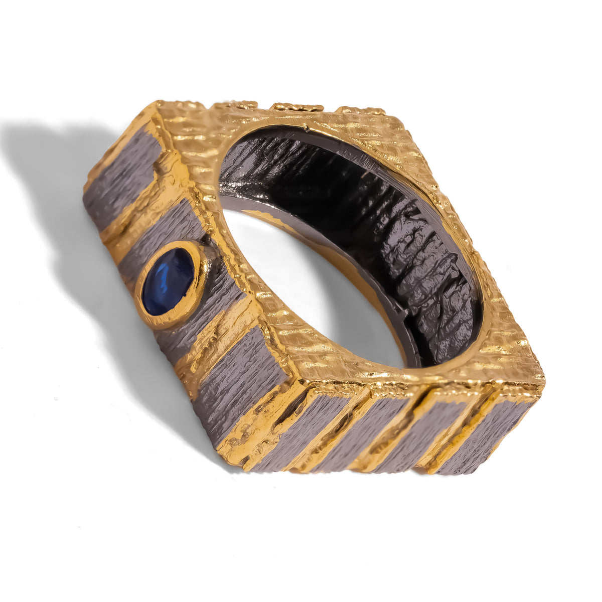 Midnight Temple two-tone ring at an angle, gold-bezel blue sapphire set between dark textured panels