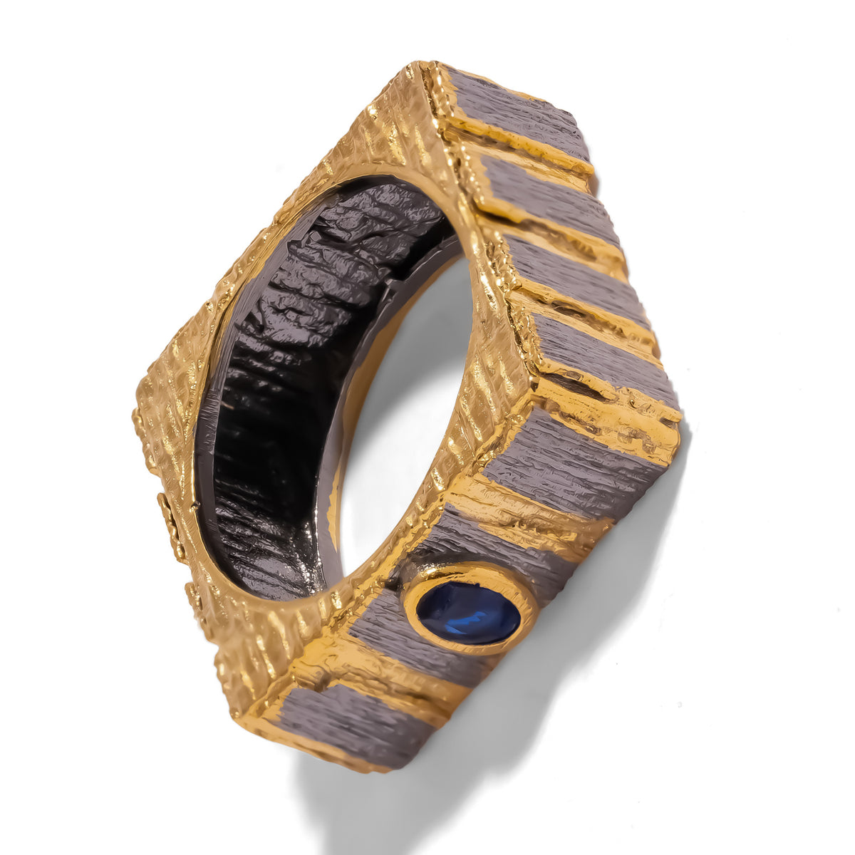 Midnight Temple Blue Sapphire Two-Tone Statement Ring tilted on white, showing the ridged gold top and gunmetal sides