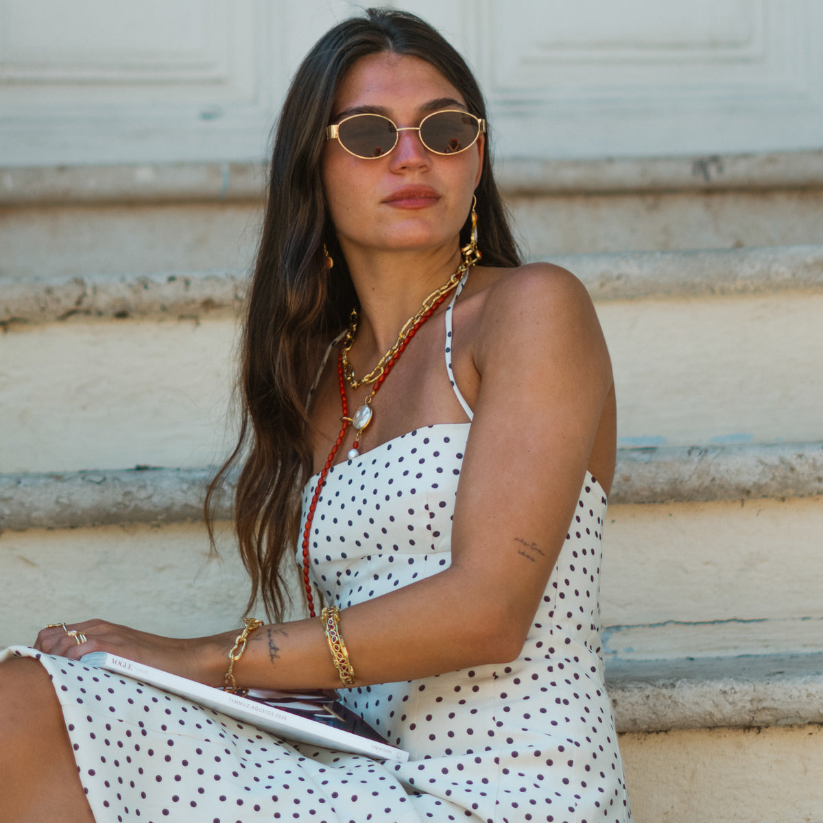 Model in a polka dot dress on stone steps wearing the Molten Gold chunky link bracelet with layered gold necklaces