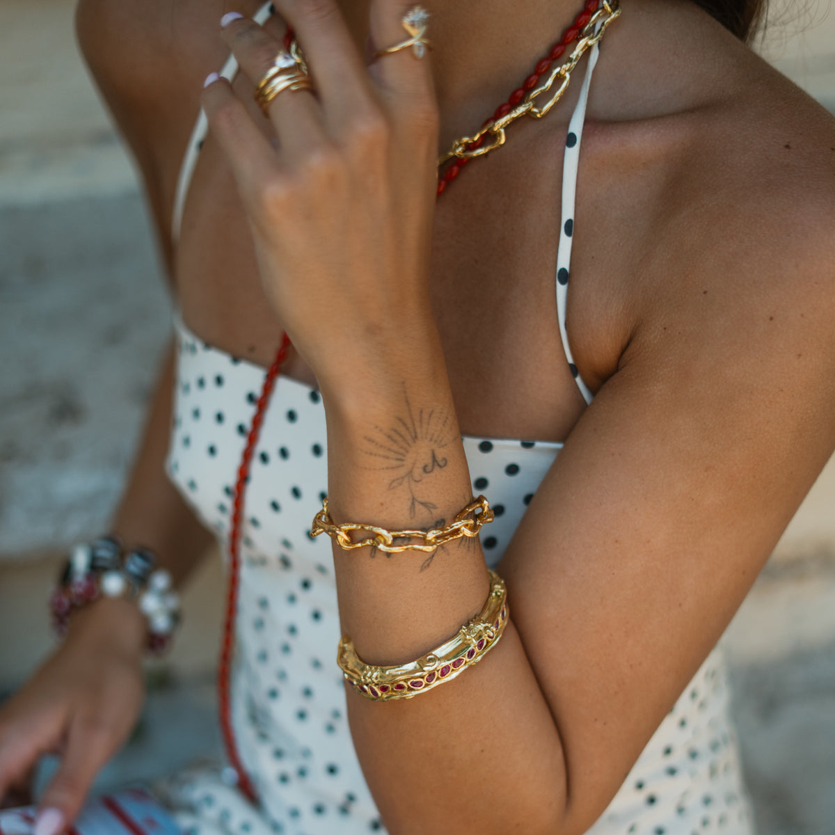 Close view of the Molten Gold chunky link bracelet stacked above a gold cuff, polka dot dress behind