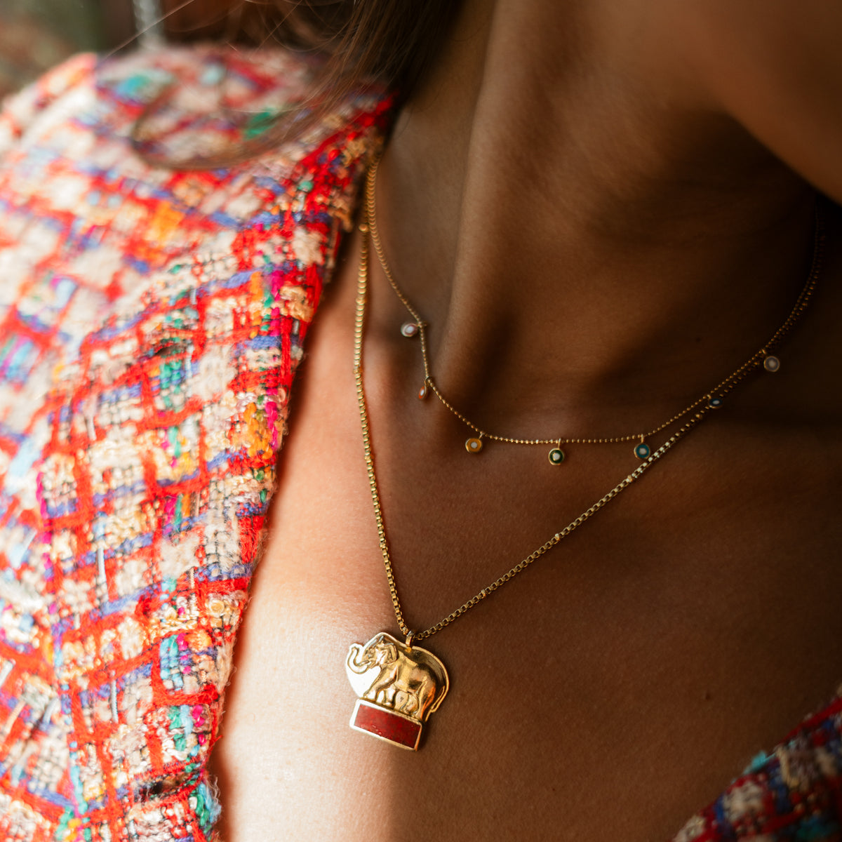Rainbow evil eye charm gold necklace worn at the collarbone with a longer gold pendant necklace