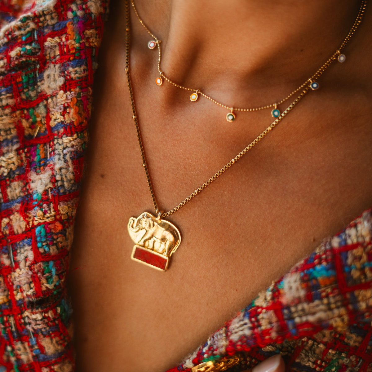 Close view of the rainbow enamel evil eye charm necklace worn high on the neck, layered with a gold elephant pendant