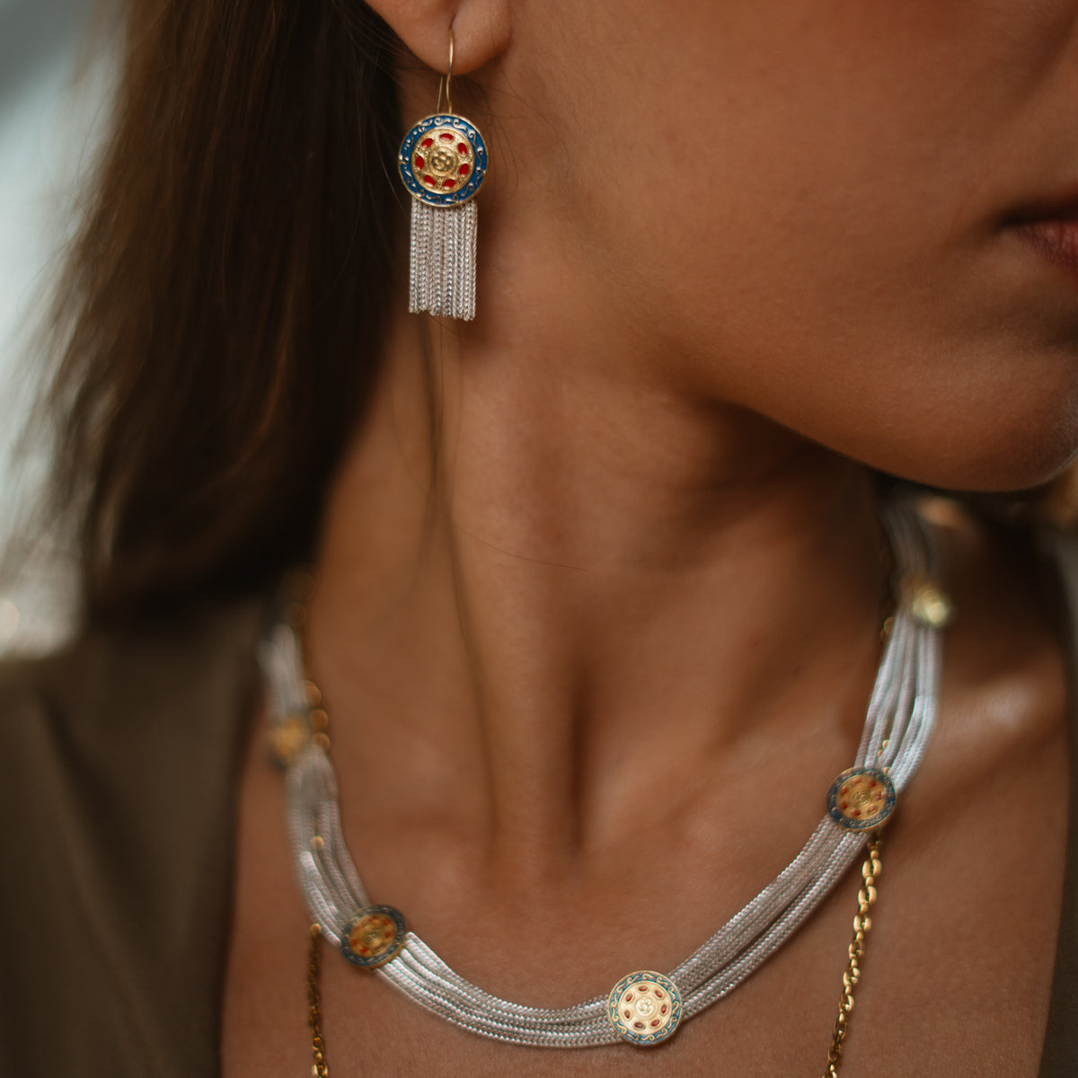 Close view of a model wearing the Mystic Bloom tassel earring with a matching woven silver necklace set with enamel medallions