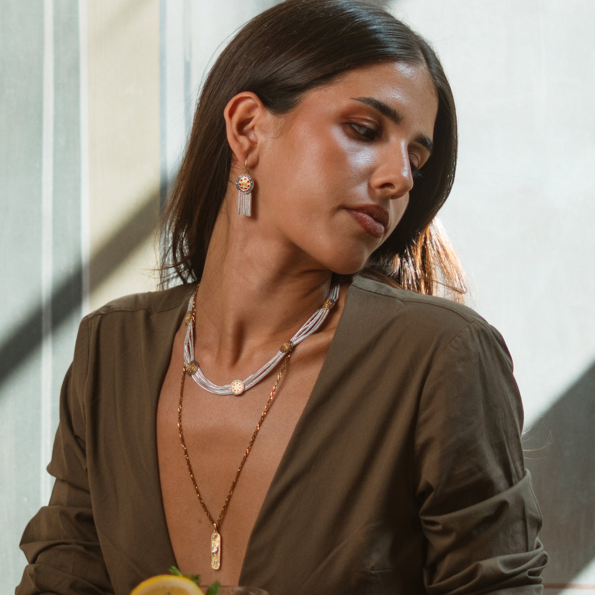 Model looking down in an olive shirt wearing the Mystic Bloom enamel tassel earring and a layered silver and gold necklace