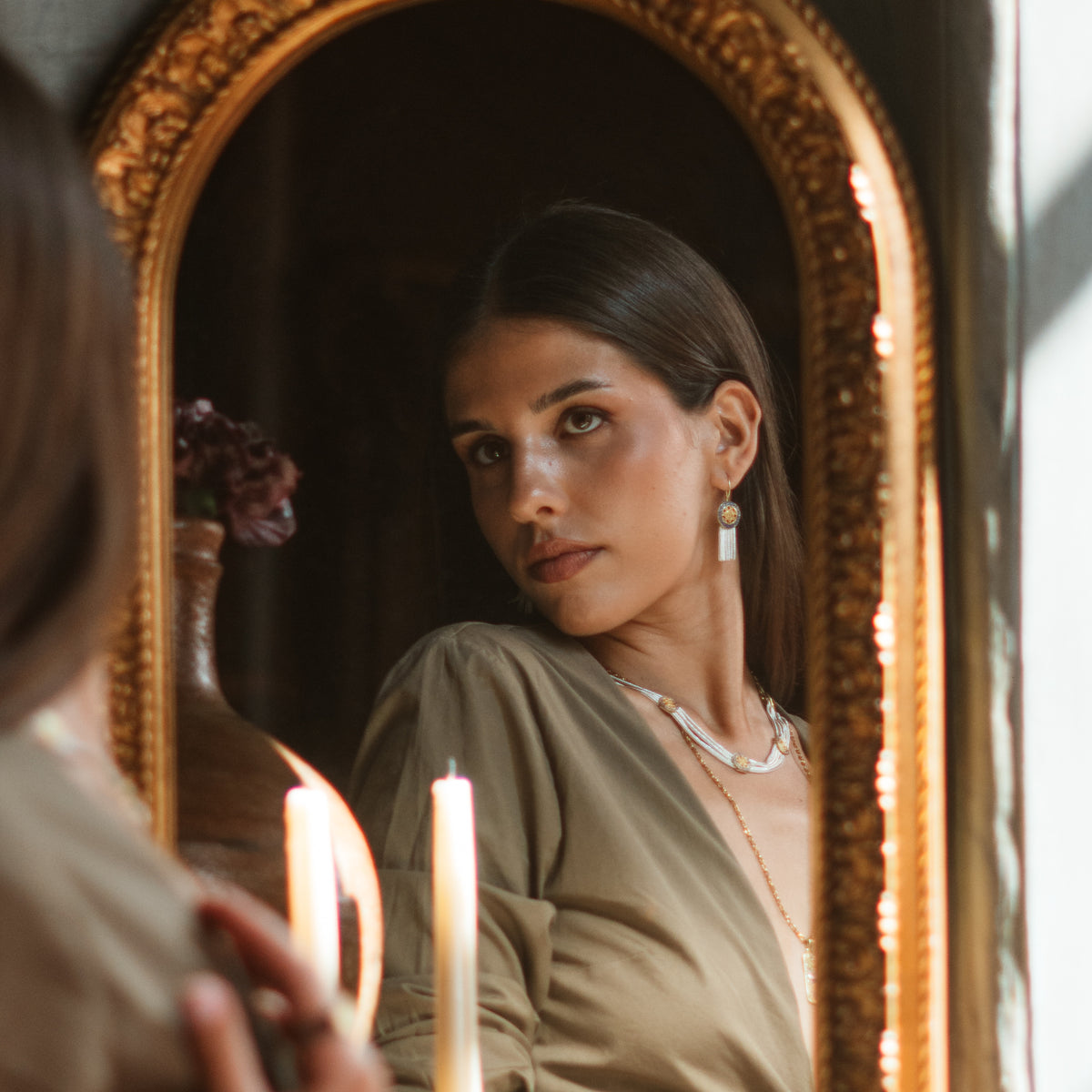 Model reflected in a gilded arched mirror by candlelight, wearing the Mystic Bloom silver tassel earrings