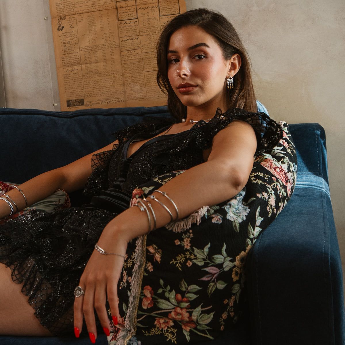 Model seated on a blue sofa wearing the Mystic Temple two tone statement earrings and silver bangles