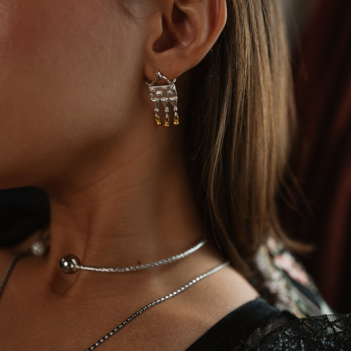 Close up of the Mystic Temple silver statement earring on the ear, gold beads swinging below the silver plate