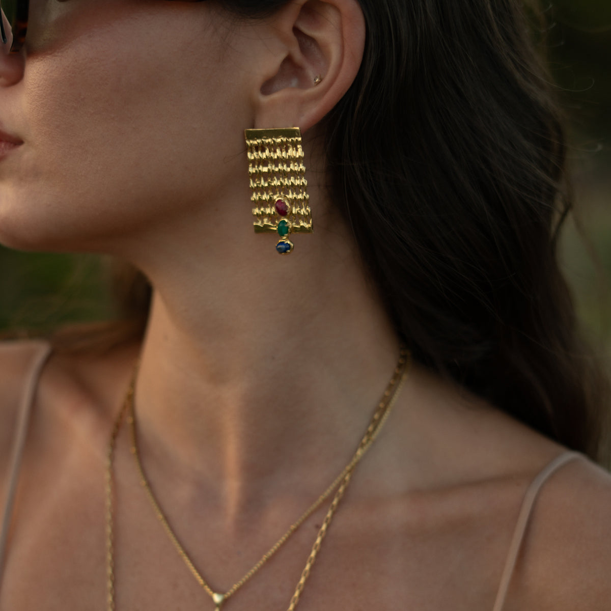 Side view of a model wearing the Mystic Trio gold statement earring, the three gemstones catching the evening light