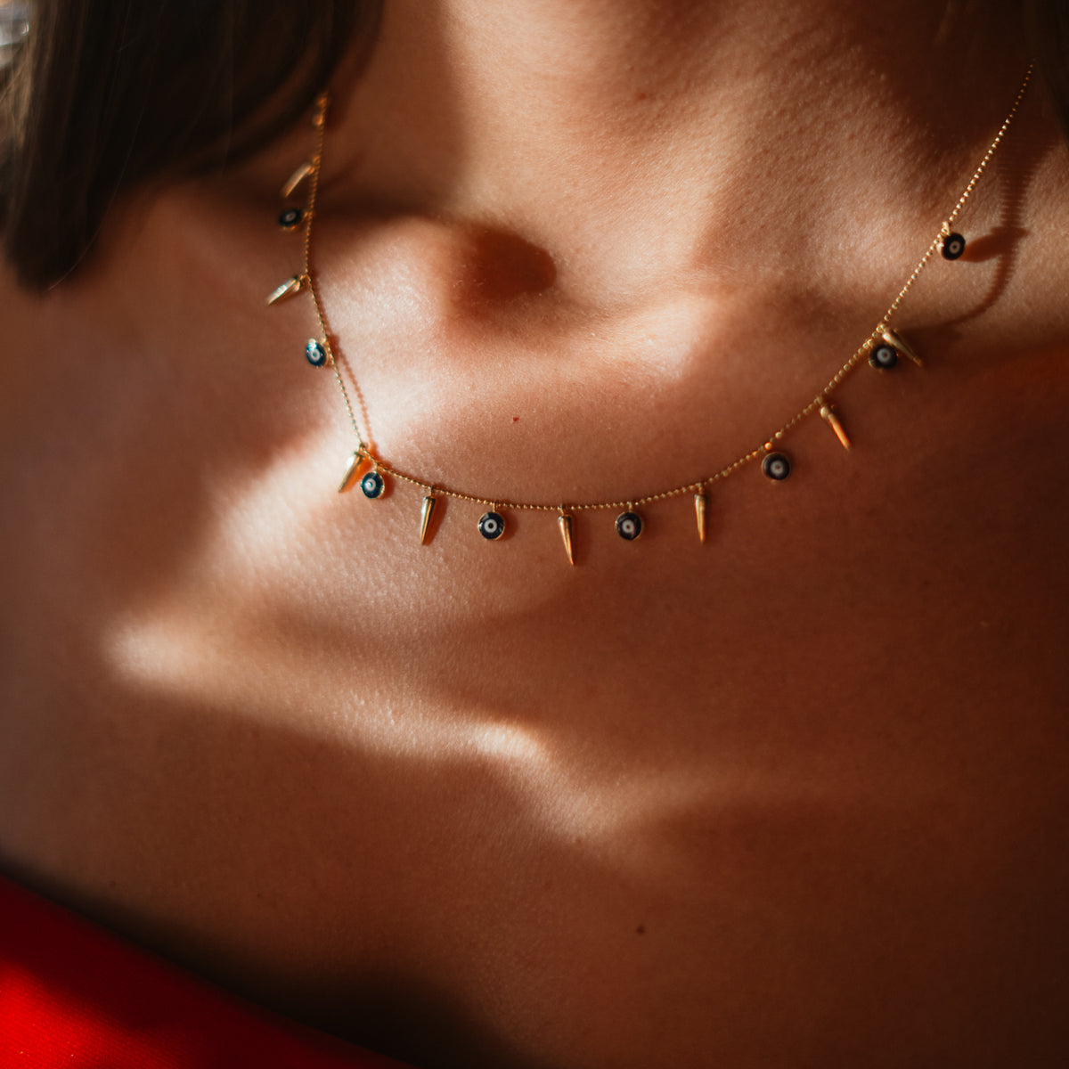 Navy blue evil eye and gold spike charm necklace worn at the base of the neck in soft shadow
