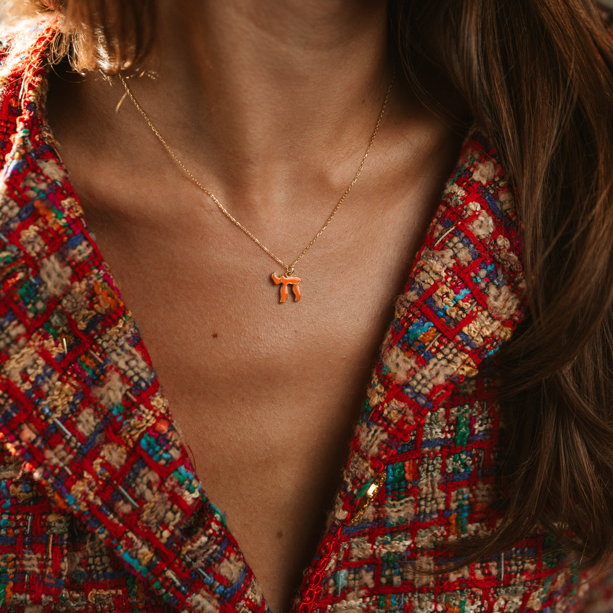 Orange enamel Chai pendant worn below the collarbone with a red tweed jacket