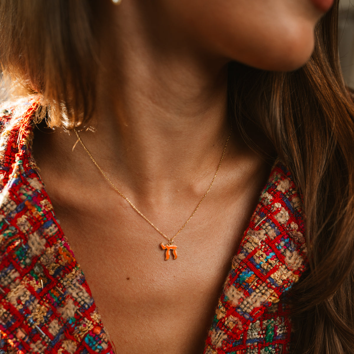 Close view of the dainty orange Chai pendant on the neck, framed by a red tweed jacket