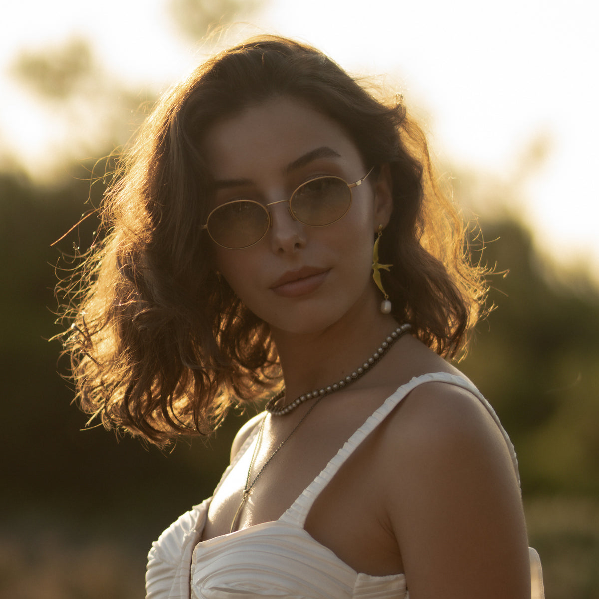 Side profile of the pearl tennis necklace worn with gold sunglasses and a pearl drop earring