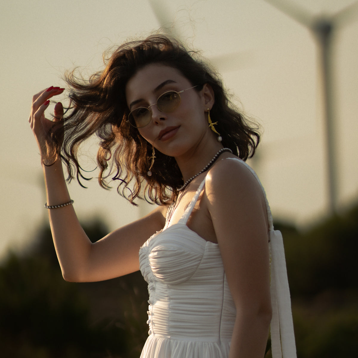 Woman in a white dress at sunset wearing the antique gold pearl tennis necklace with gold sparrow drop earrings