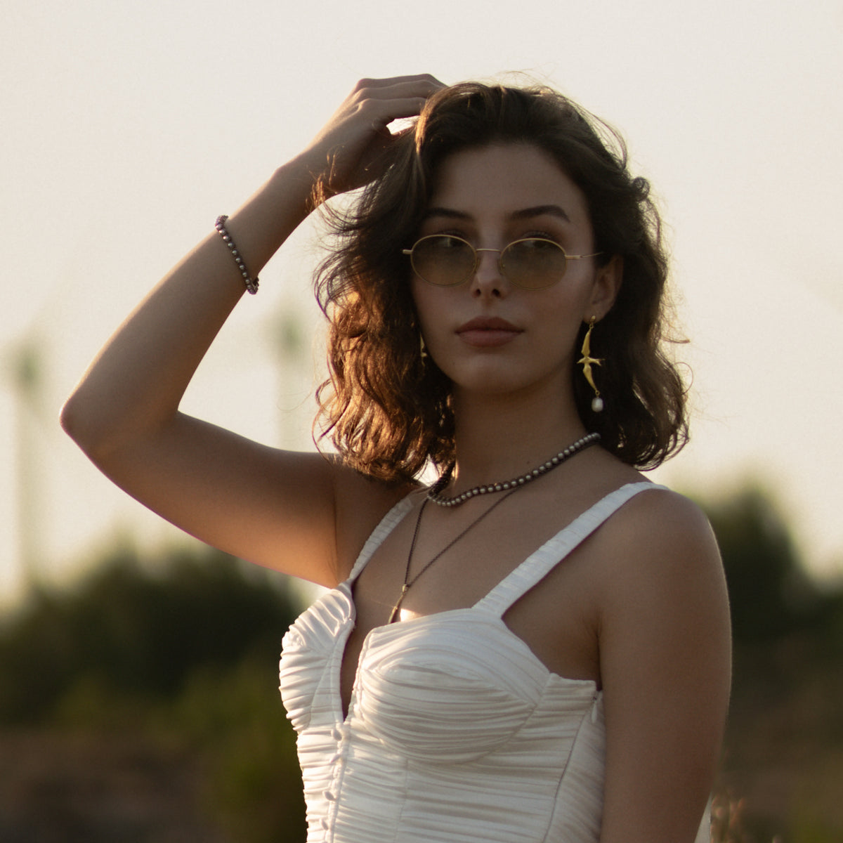 Woman outdoors wearing the pearl tennis necklace layered with a gold pendant chain and a beaded bracelet