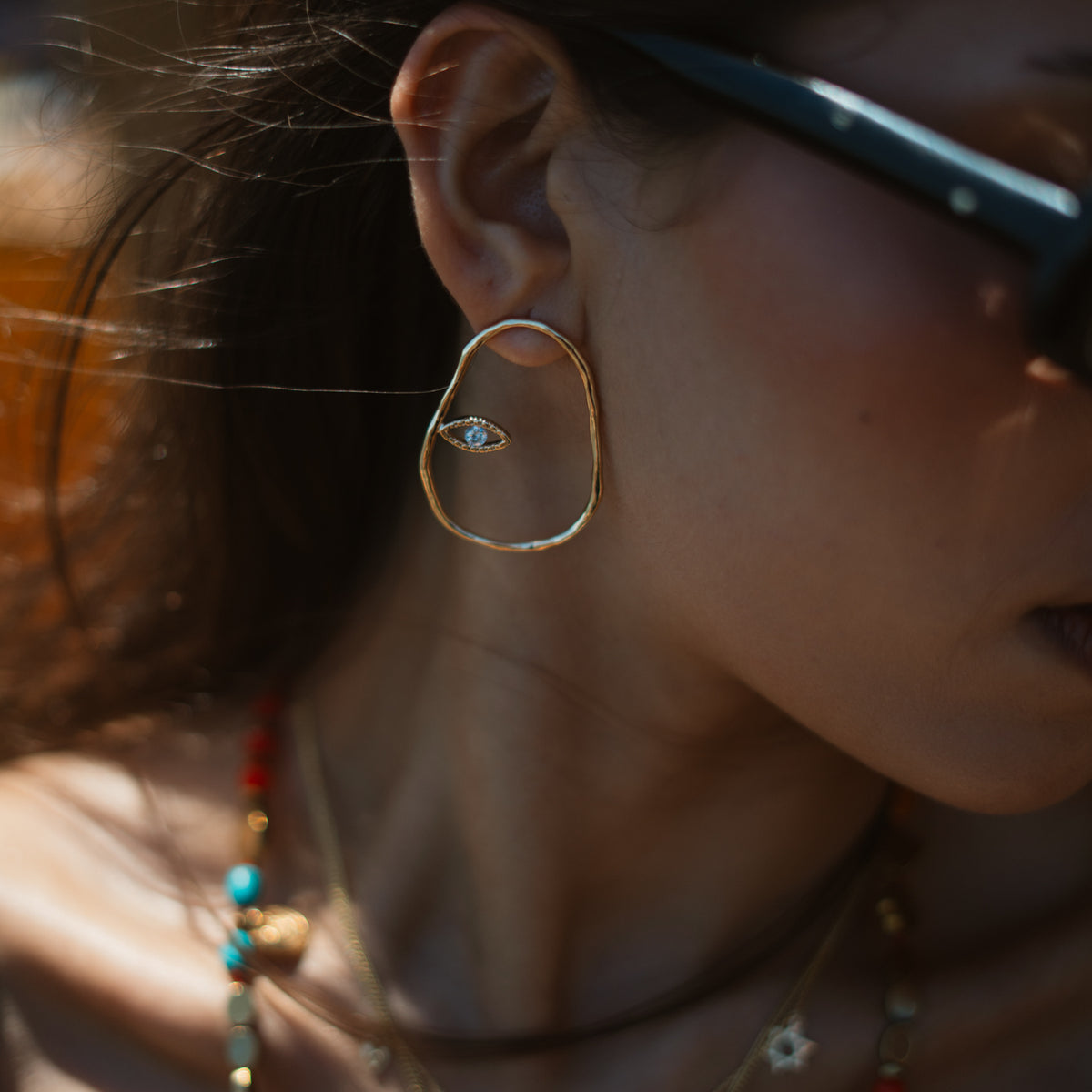 Close view of the Protective Halo Evil Eye hoop earring worn forward against the ear in sunlight