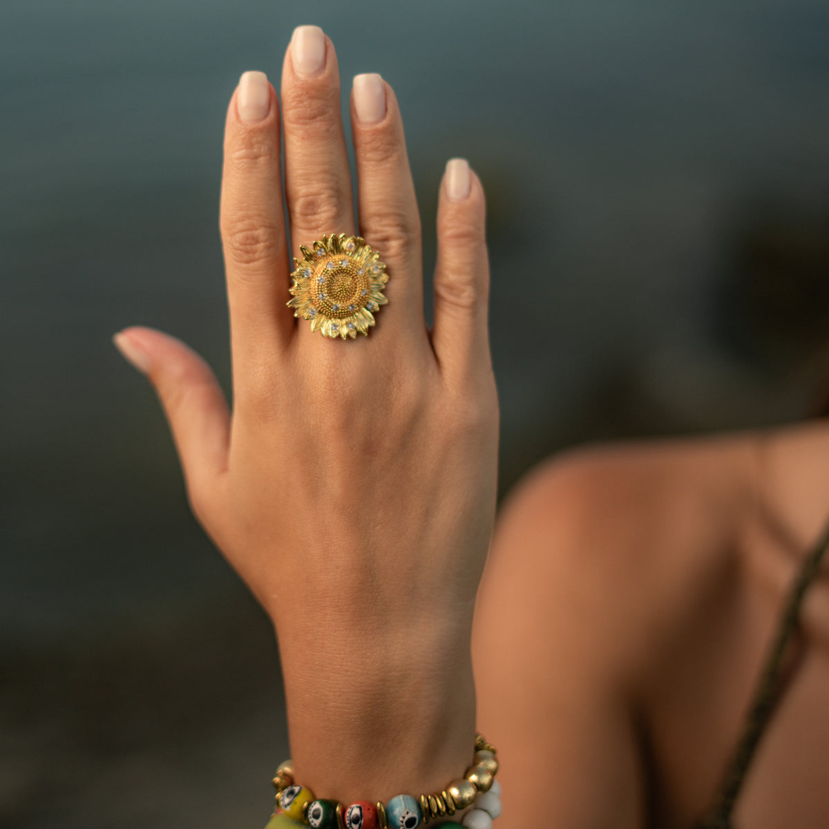 Hand raised against the sea wearing the Radiant Sunflower gold adjustable statement ring