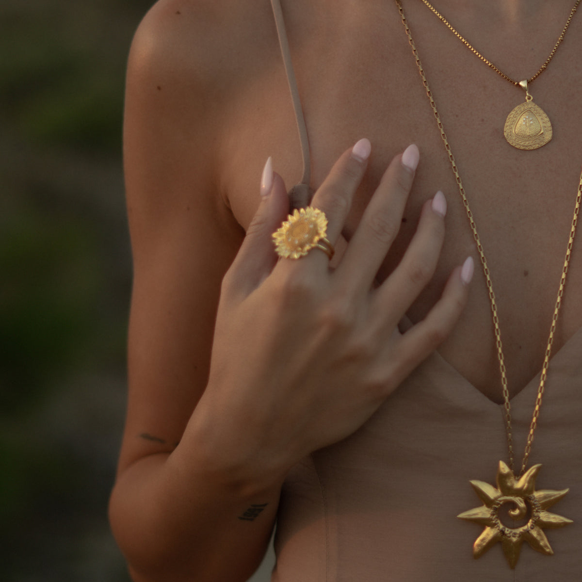 Detail of the Radiant Sunflower gold ring worn with a gold sun pendant and coin necklace