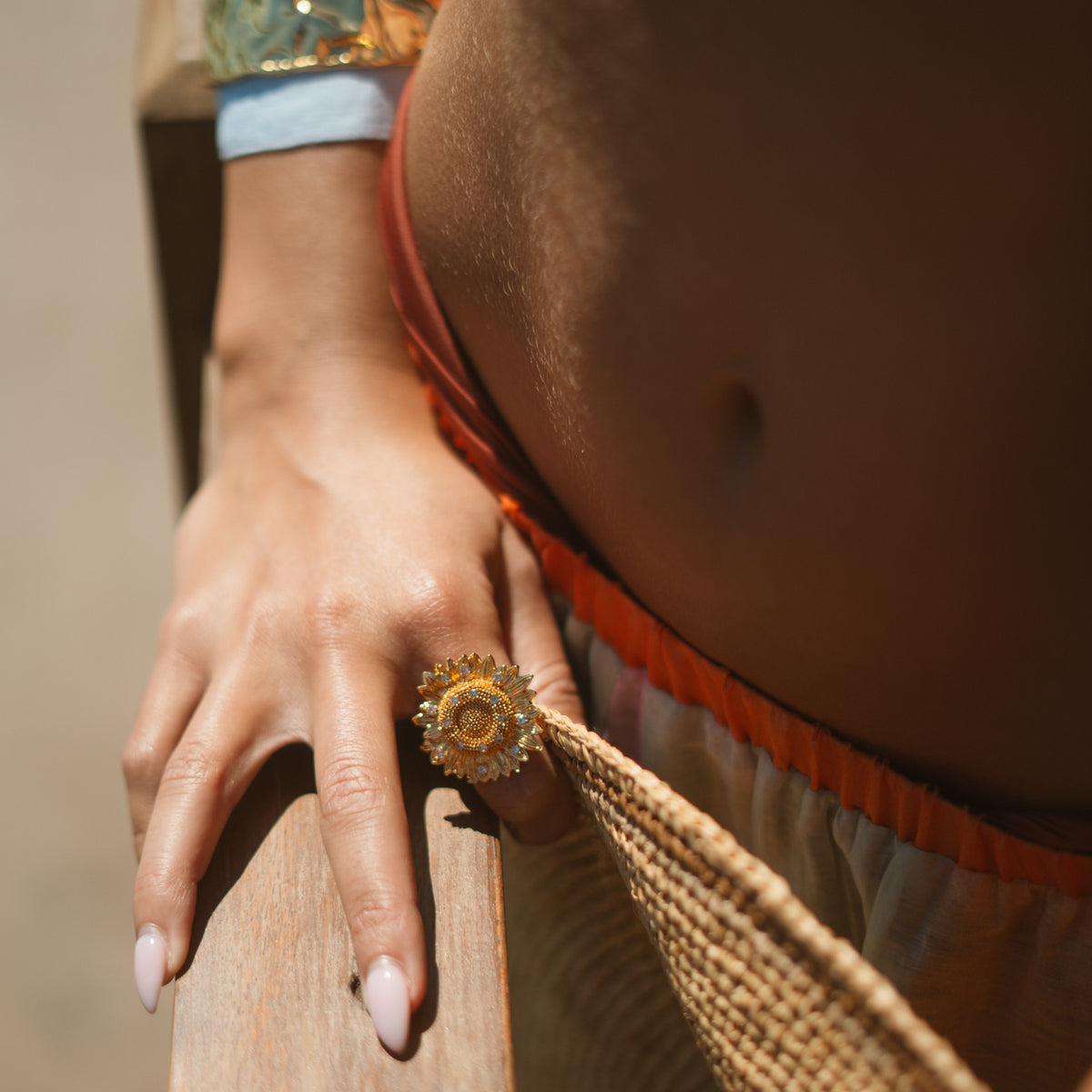 Close up of the gold sunflower statement ring worn on the hand beside a woven straw bag