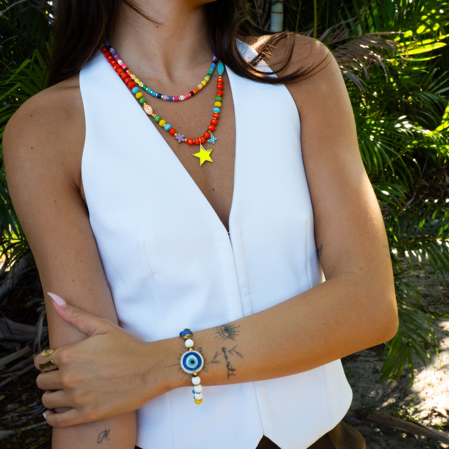 Woman wearing Reversible Evil Eye Beaded Summer Bracelet with colorful star necklace, styled with white vest — two-sided protection jewelry