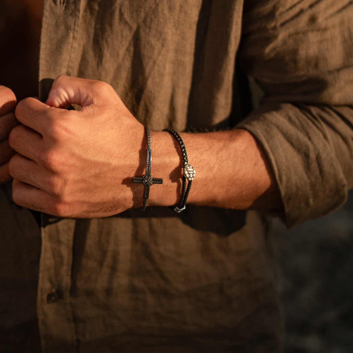 Man in an olive linen shirt wearing the ruby eye snake cord bracelet stacked with an oxidized silver cross cuff