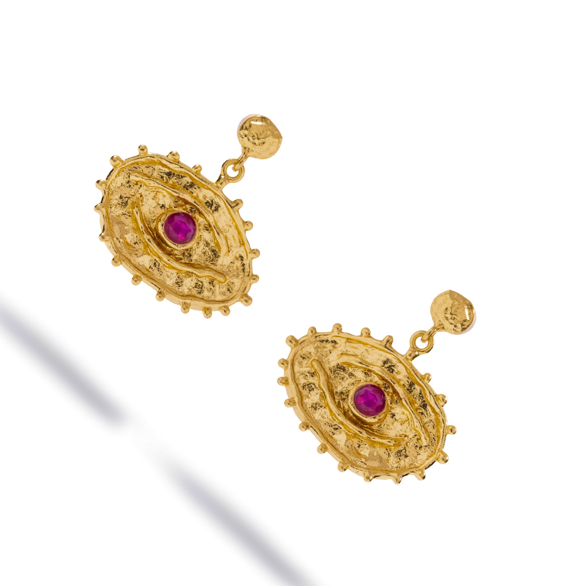 Angled studio view of the ruby evil eye gold drop earrings showing the hammered stud tops and the raised gold bead rim