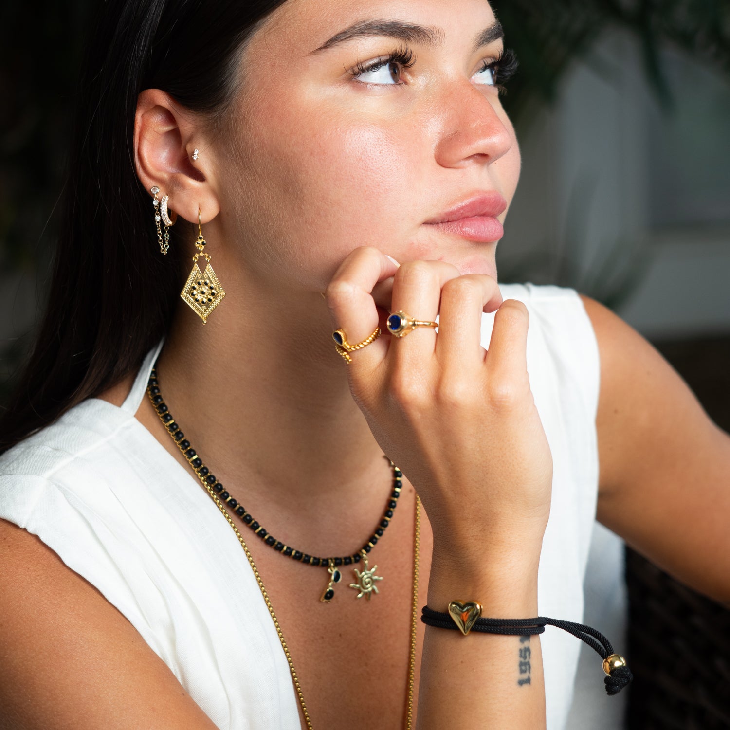 Woman wearing gold earrings, necklace, ring, and bracelet with a neutral background