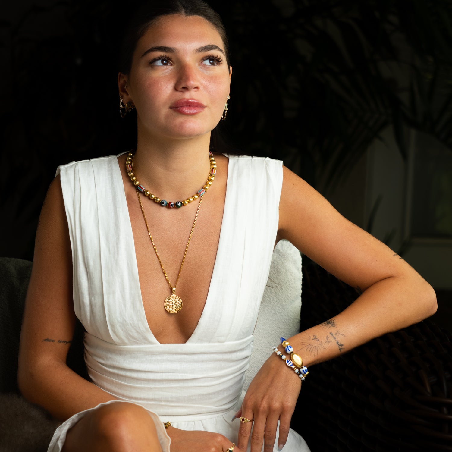 Woman wearing sacred Om Flower of Life talisman gold necklace with white linen dress