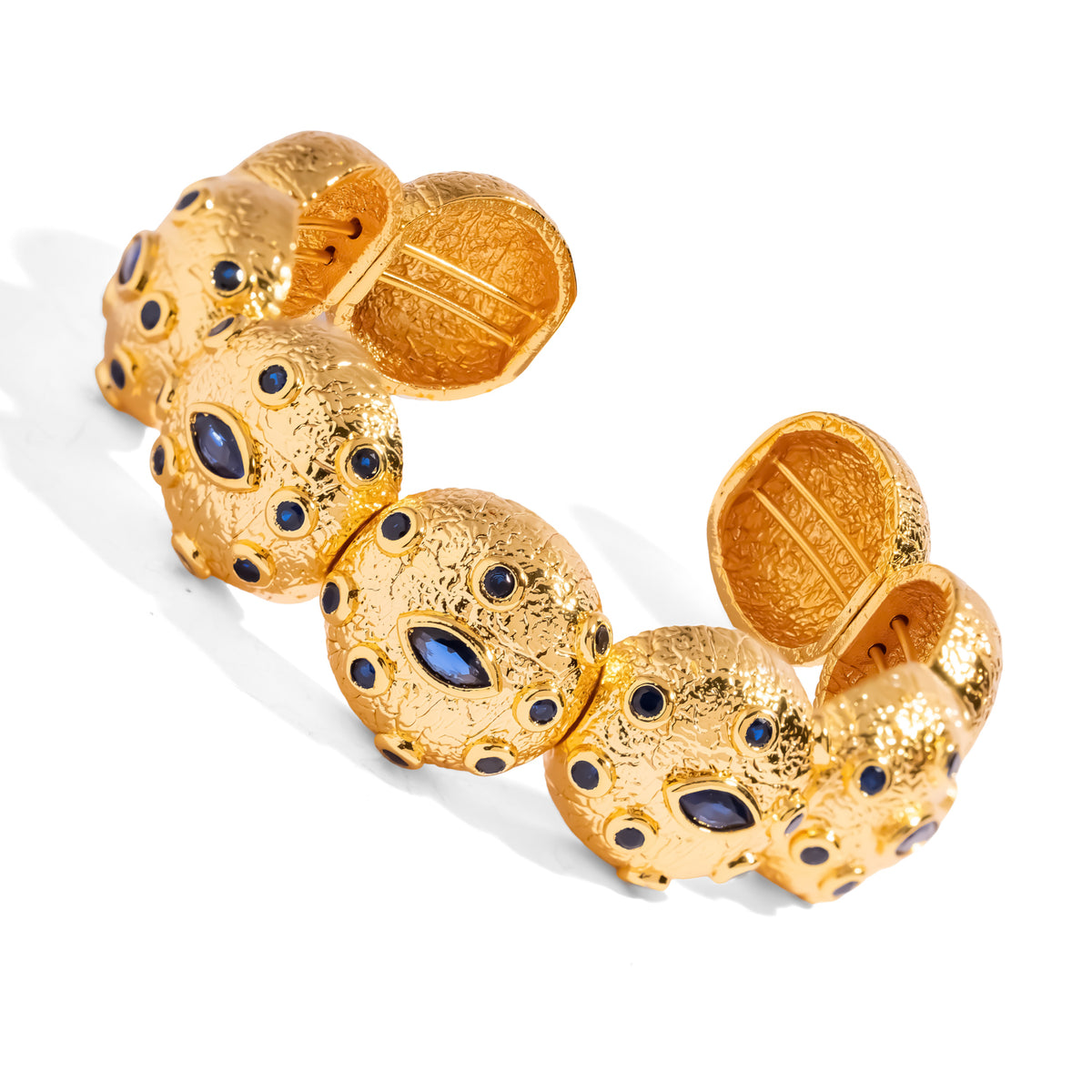 Angled view of the gold cuff bracelet showing the open ends and the hand set blue zircon eyes on each textured dome