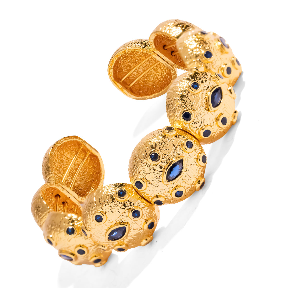 Gold cuff bracelet viewed from above, showing the linked domes, the marquise blue zircon eyes and the inside of the open ends