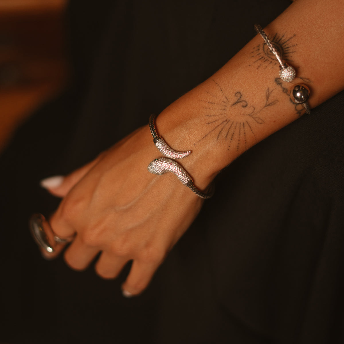Close view of the serpent emerald eye pave silver cuff on the wrist with a silver ball cuff and a sculptural silver ring