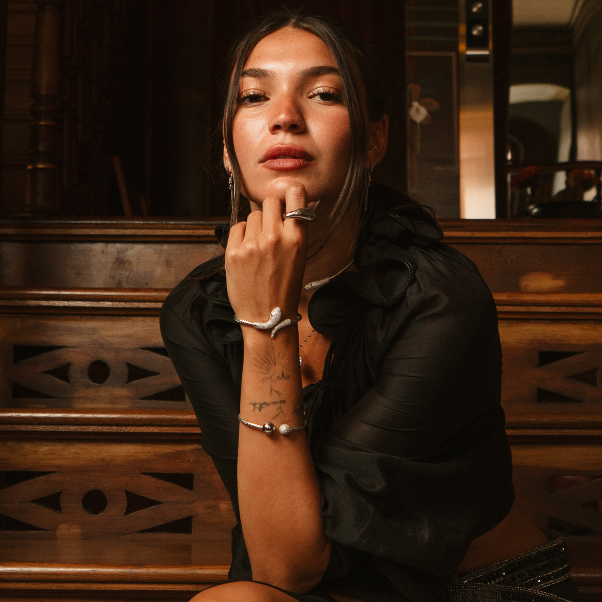 Model in a black blouse on a wooden staircase wearing the serpent pave sterling silver cuff and a silver ball cuff