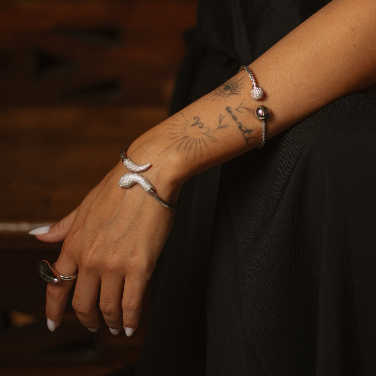 Model in black wearing the serpent pave silver cuff at the wrist and a pave ball cuff on the forearm