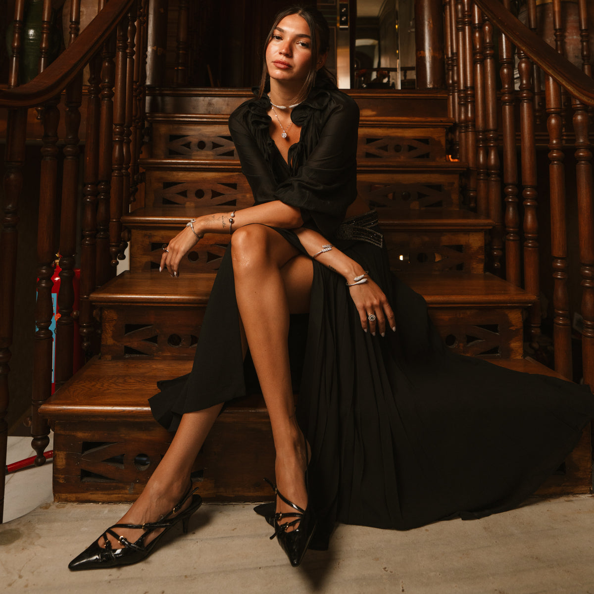Full length view of a model in black seated on stairs wearing the twin serpent pave silver cuff