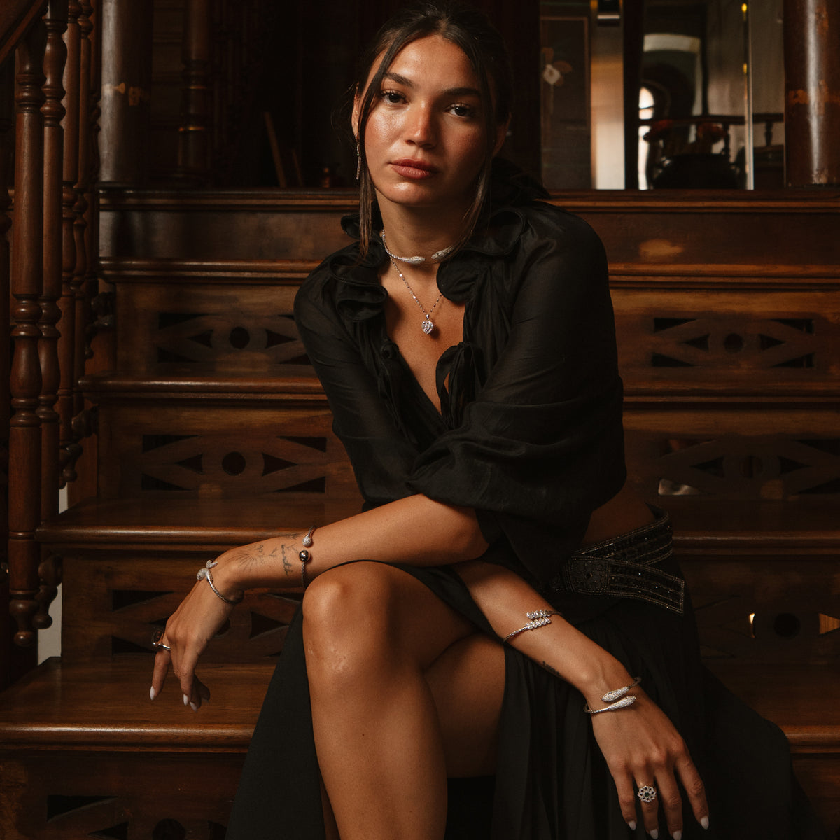 Woman in black seated on stairs wearing the woven silver serpent collar and silver bracelets