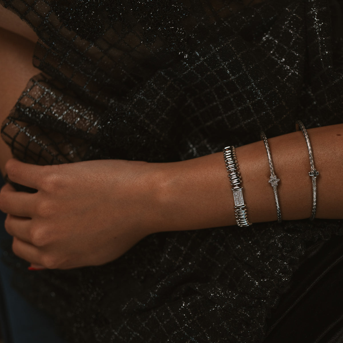 Silver Rhythm link bracelet worn with two slim silver bangles, hand resting on black sparkle fabric