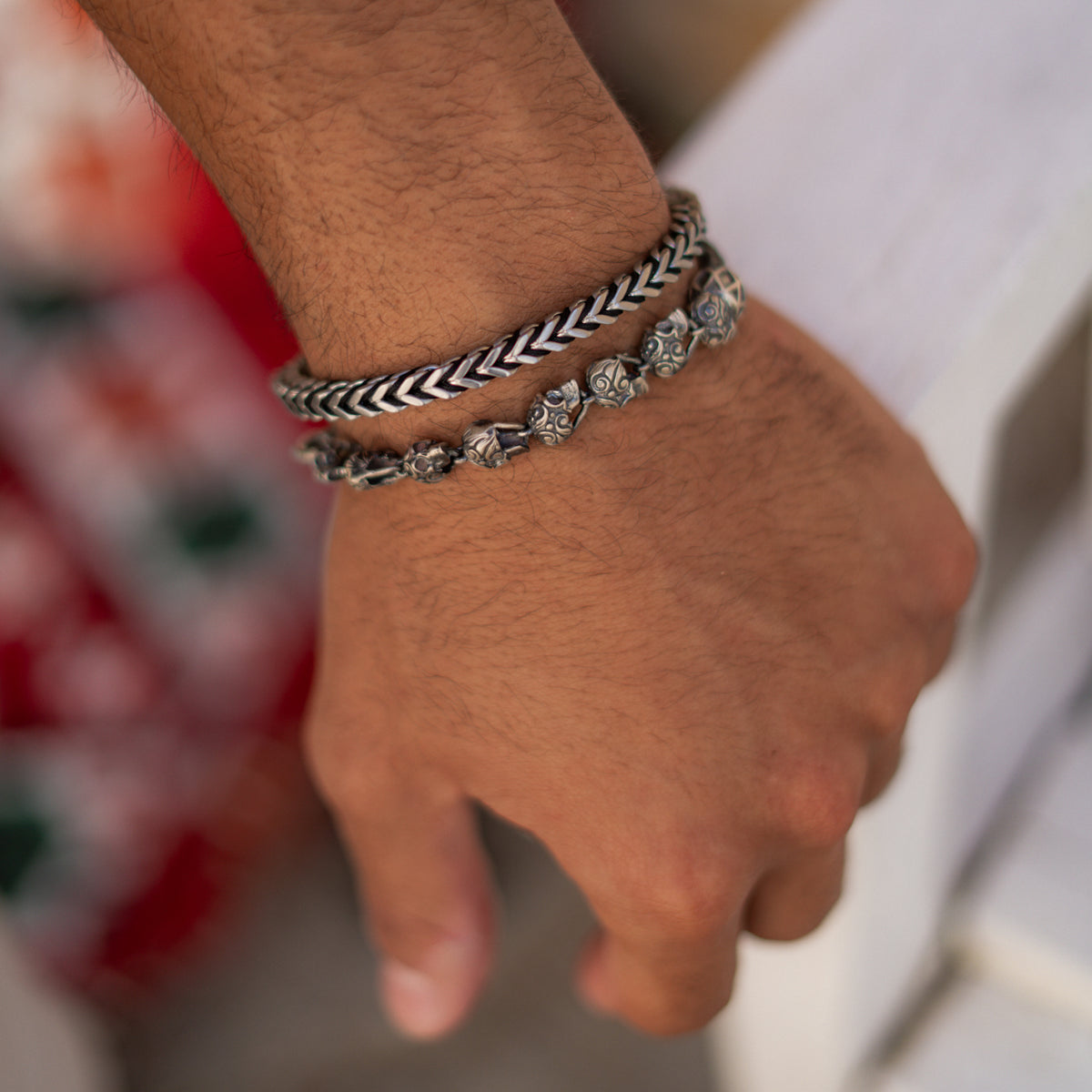 Skull bead braided silver bracelet stacked with a chevron chain bracelet on a man's wrist, resting on a white railing