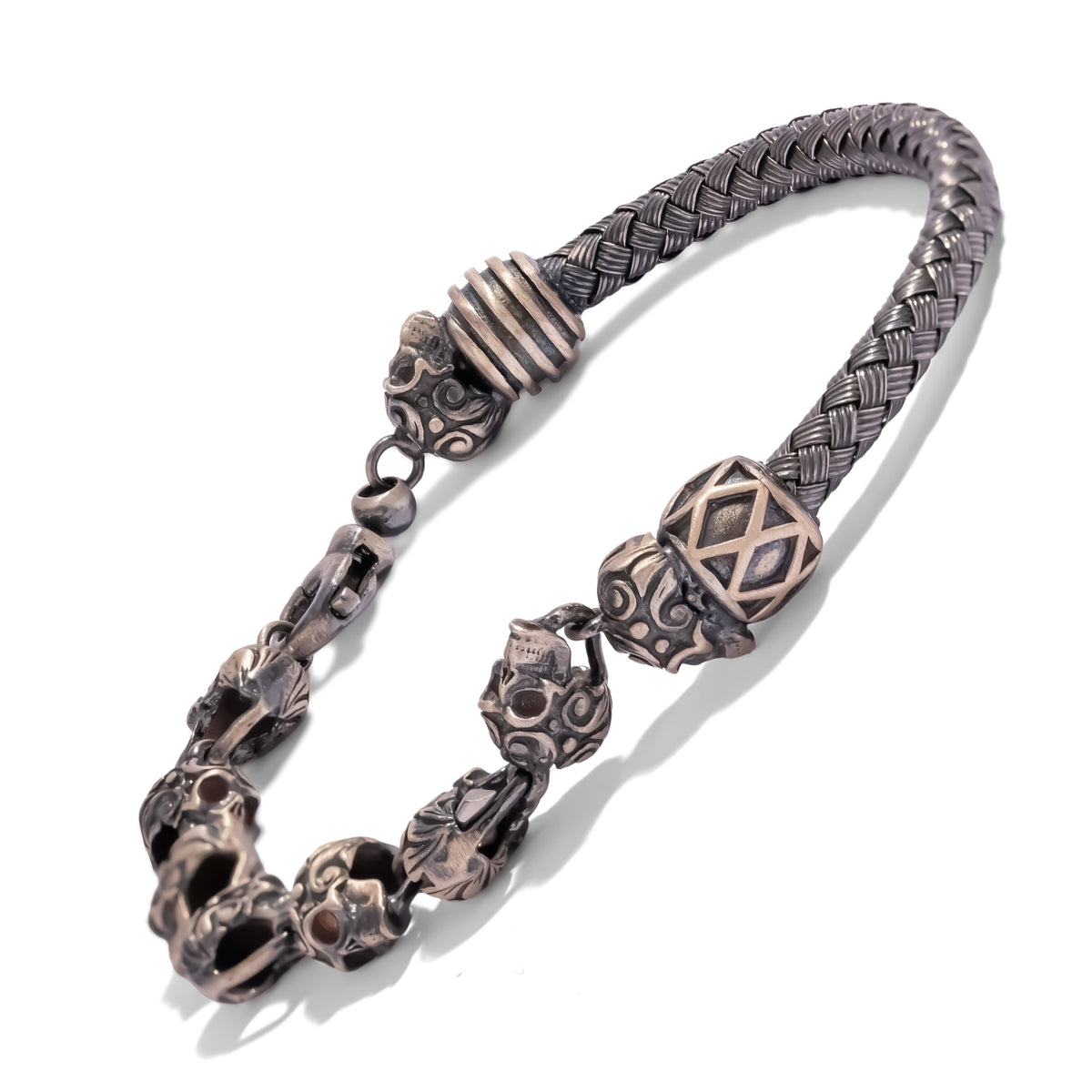 Oxidized sterling silver bracelet seen from above, the braided band leading into a chain of scroll engraved skulls