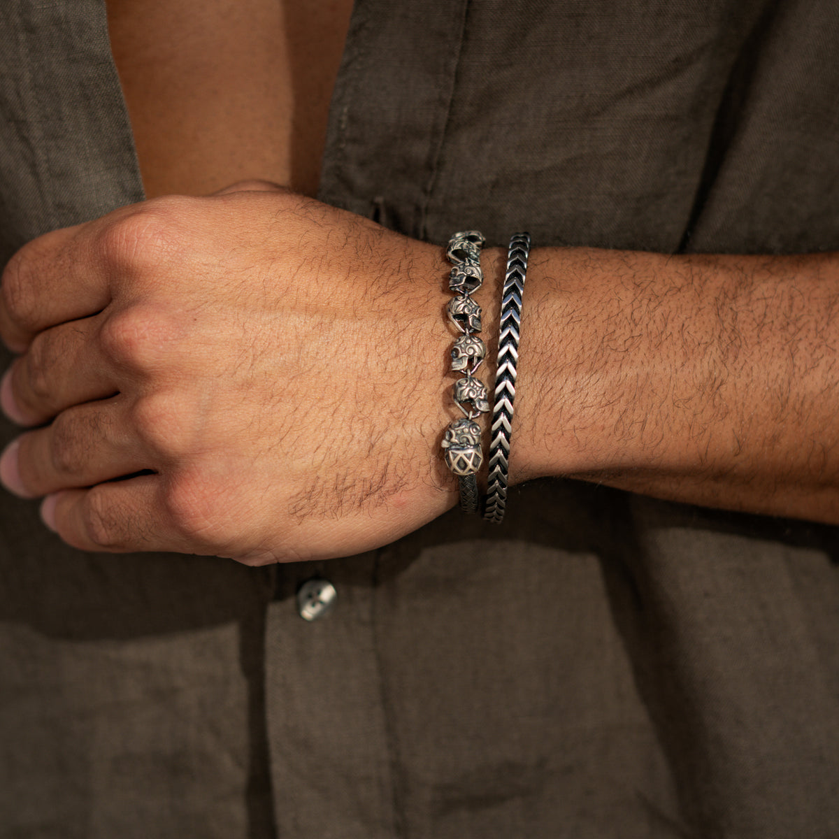 Man in a linen shirt wearing the oxidized silver skull link bracelet with a chevron chain bracelet